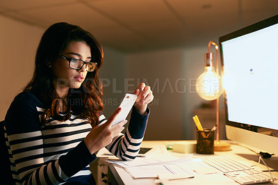 Buy stock photo Shot of a young businesswoman texting on her cellphone while working late in an office