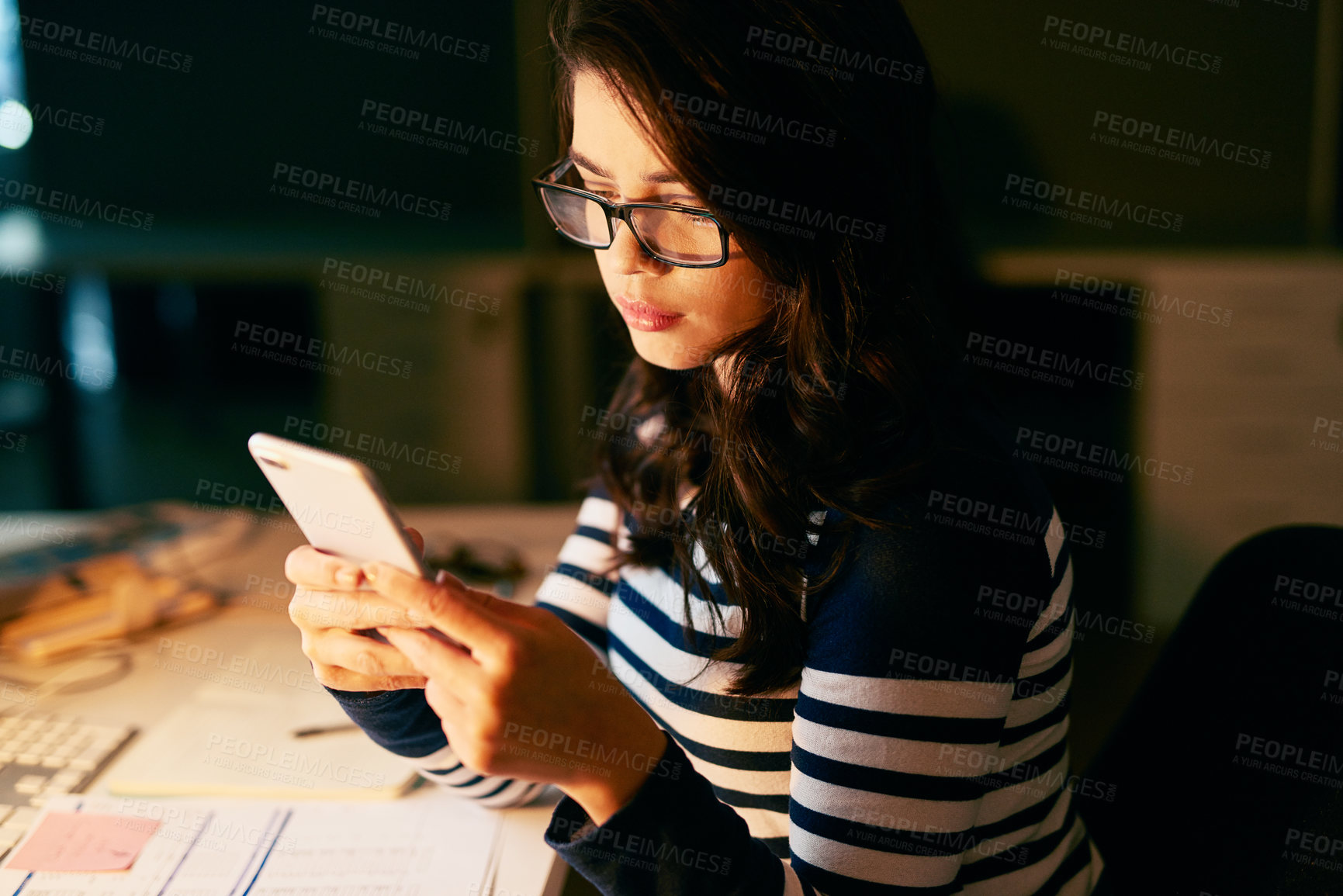 Buy stock photo Shot of a young businesswoman texting on her cellphone while working late in an office