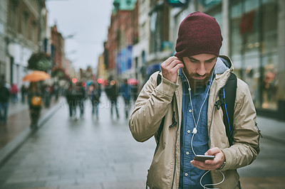 Buy stock photo Cropped shot of a handsome young man listening to music on his cellphone while walking through the city