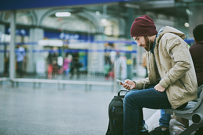 Buy stock photo Cropped shot of a handsome young man listening to music on his cellphone while sitting in a bus station