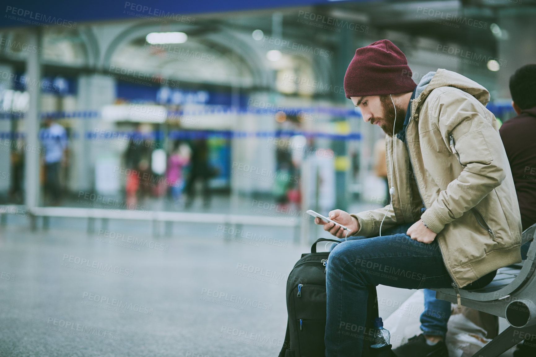 Buy stock photo Cropped shot of a handsome young man listening to music on his cellphone while sitting in a bus station