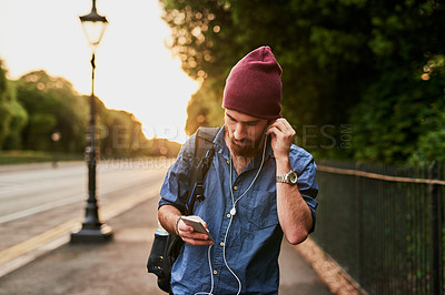 Buy stock photo Cropped shot of a handsome young man listening to music on his cellphone while walking through the city