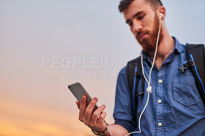 Buy stock photo Low angle shot of a handsome young man listening to music on his cellphone while walking through the city