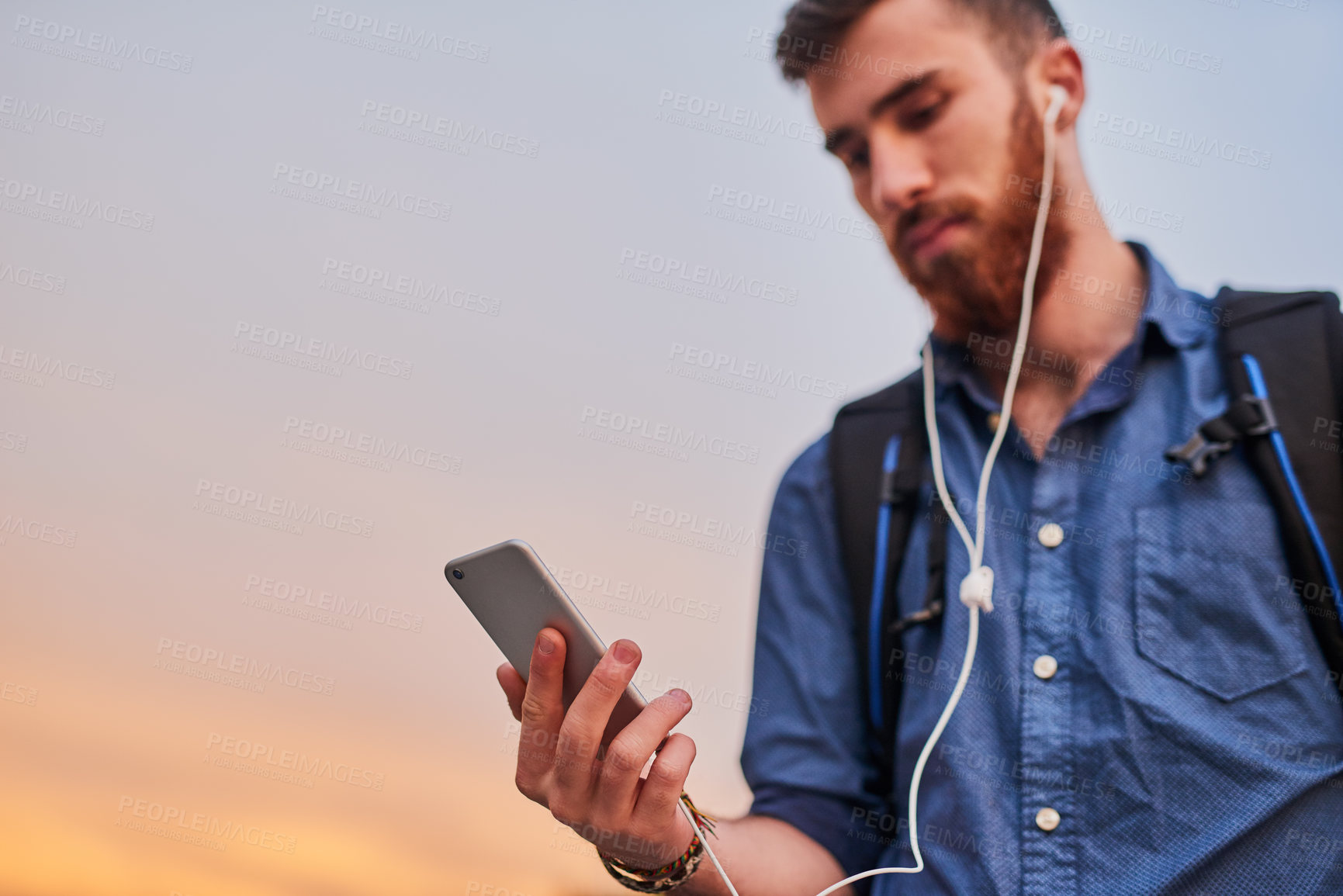 Buy stock photo Low angle shot of a handsome young man listening to music on his cellphone while walking through the city