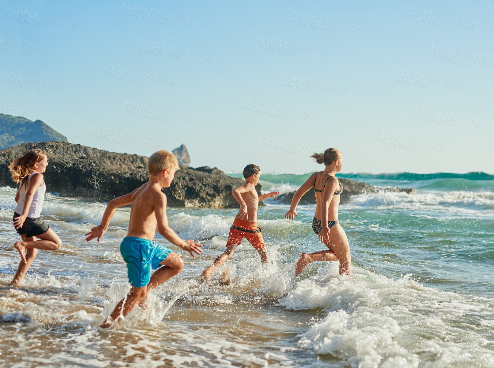 Buy stock photo Shot of siblings running into the water at the beach on a sunny day