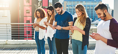 Buy stock photo Cropped shot of a group of young people texting on their cellphones while standing outdoors