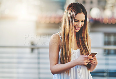 Buy stock photo Cropped shot of an attractive young woman sending a text message while standing outside