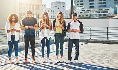 Buy stock photo Full length shot of a group of young people texting on their cellphones while standing outdoors