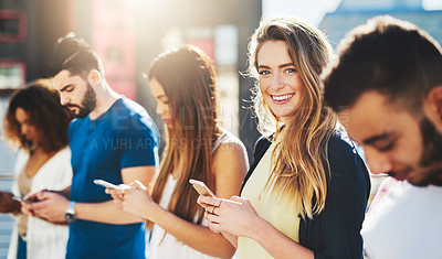 Buy stock photo Cropped portrait of an attractive young woman sending a text message while standing outside with a group of friends