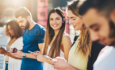 Buy stock photo Cropped portrait of an attractive young woman sending a text message while standing outside with a group of friends