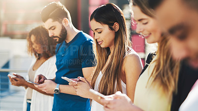 Buy stock photo Cropped shot of an attractive young woman sending a text message while standing outside with a group of friends