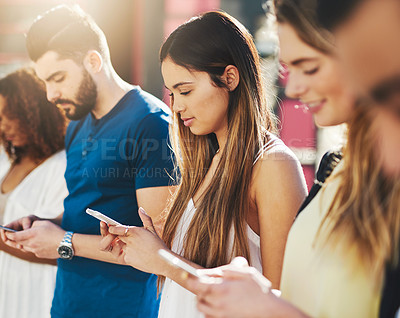 Buy stock photo Cropped shot of an attractive young woman sending a text message while standing outside with a group of friends