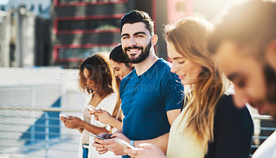 Buy stock photo Cropped portrait of a handsome young man sending a text message while standing outside with a group of friends