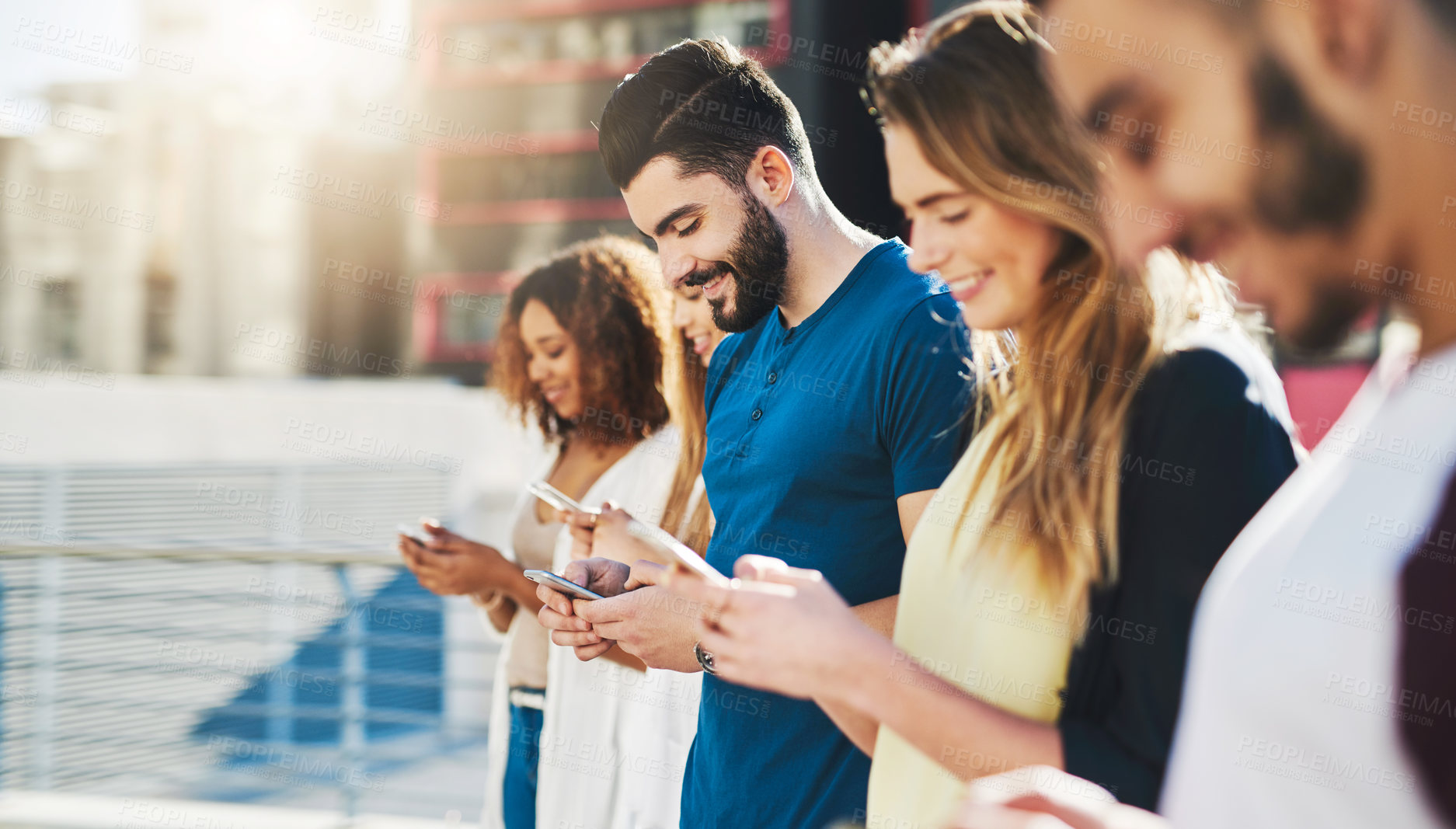 Buy stock photo Cropped shot of a handsome young man sending a text message while standing outside with a group of friends