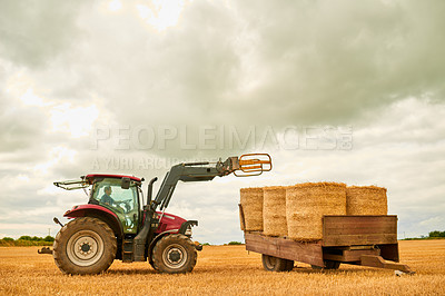 Buy stock photo Hay, countryside and a tractor on a farm for sustainability outdoor on an open field during the harvest season. Agriculture, sky and clouds with a red industrial farming vehicle harvesting in nature