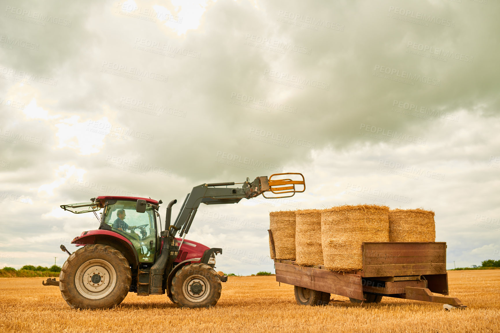 Buy stock photo Hay, countryside and a tractor on a farm for sustainability outdoor on an open field during the harvest season. Agriculture, sky and clouds with a red industrial farming vehicle harvesting in nature