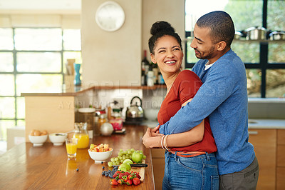Buy stock photo Cropped shot of a handsome young man embracing his wife while she makes a fruit salad in the kitchen