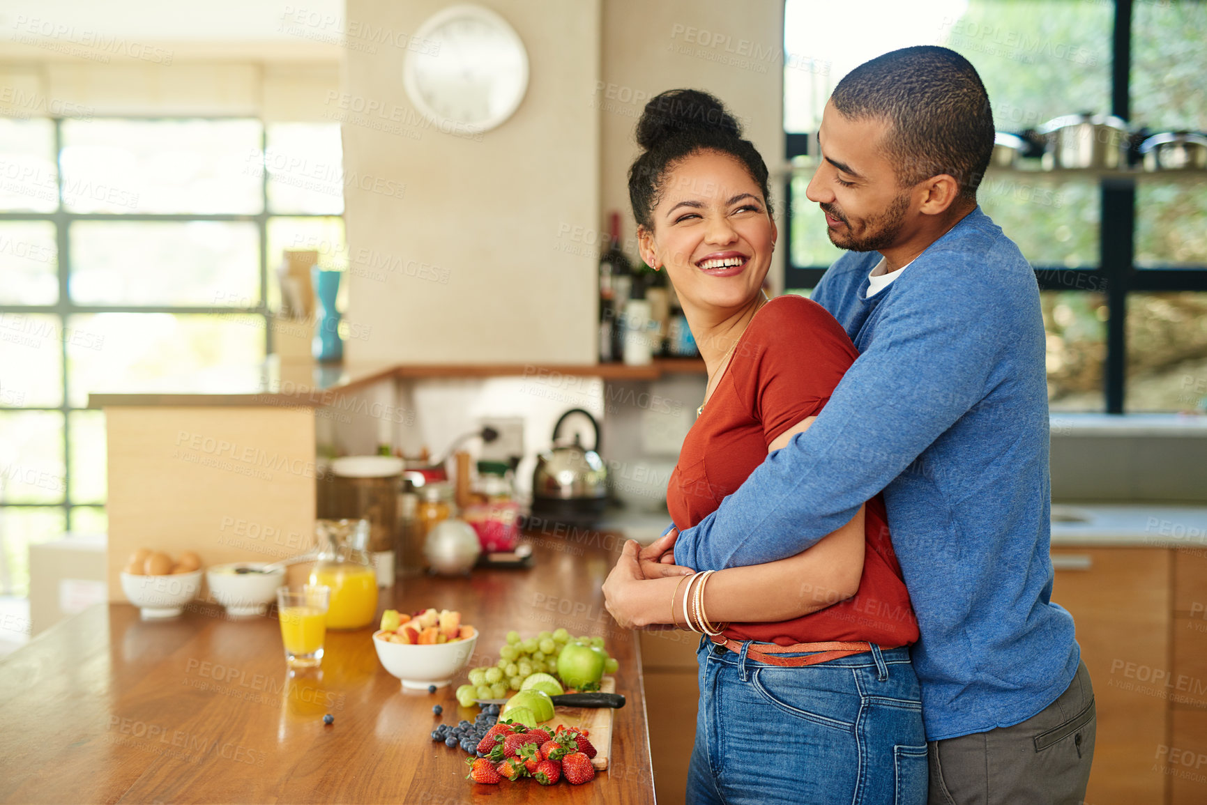 Buy stock photo Cropped shot of a handsome young man embracing his wife while she makes a fruit salad in the kitchen