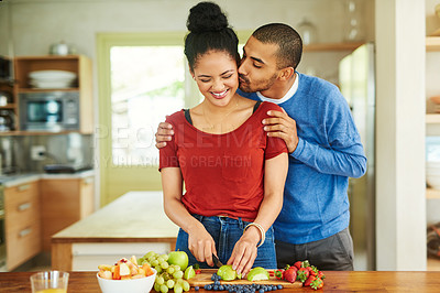 Buy stock photo Cropped shot of a handsome young man kissing his wife while she makes a fruit salad in the kitchen