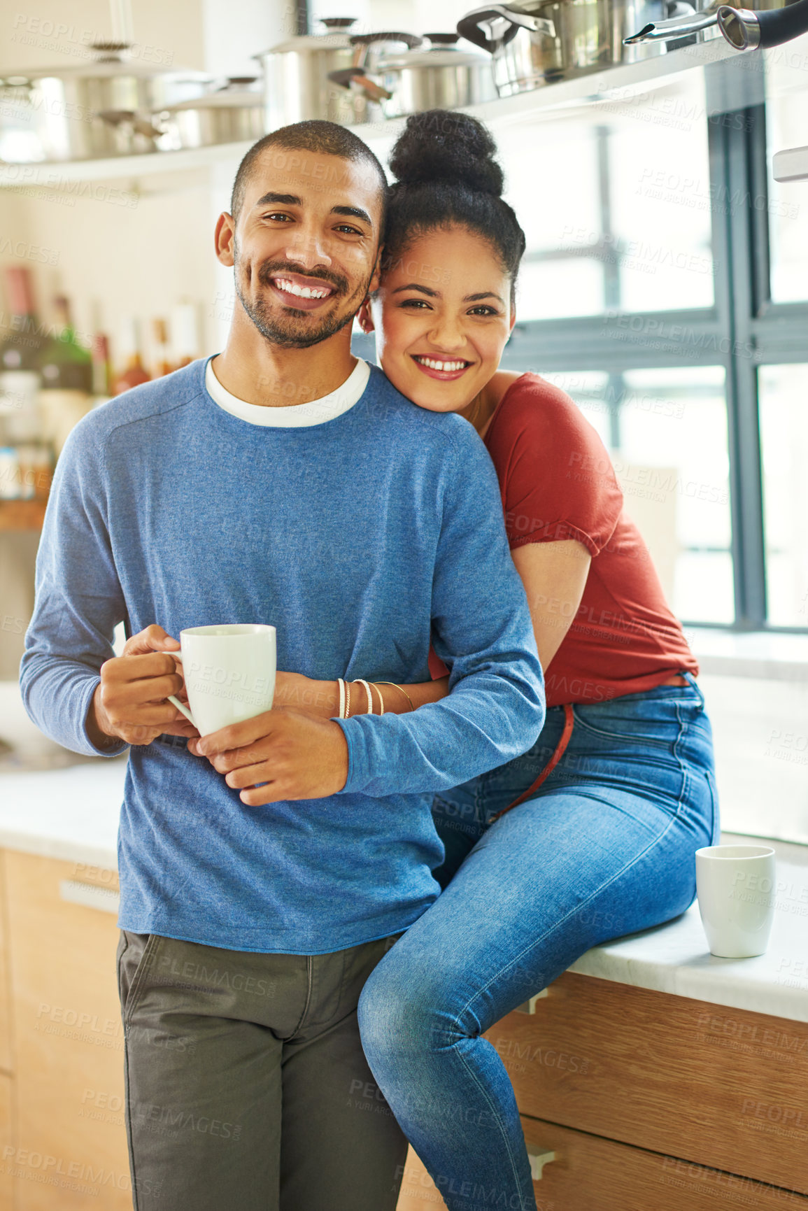 Buy stock photo Cropped portrait of an attractive young woman embracing her husband while he drinks coffee in the kitchen