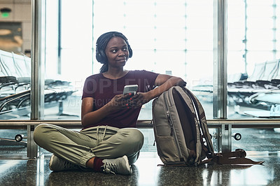 Buy stock photo Shot of a young woman listening to music on her phone while sitting at the airport