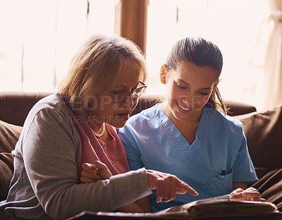 Buy stock photo Shot of a nurse and a senior woman looking at a photo album together