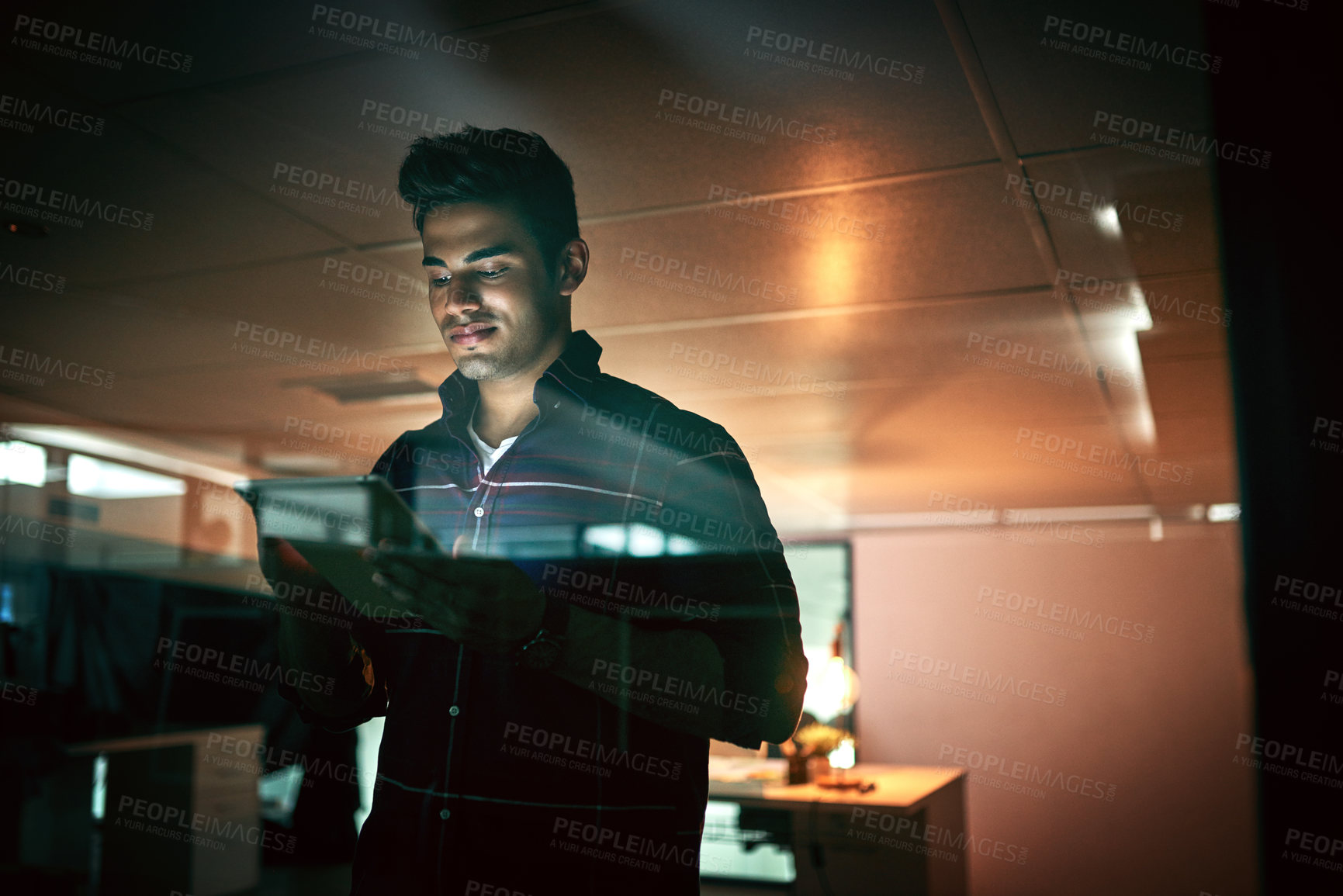 Buy stock photo Shot of a young businessman using a digital tablet during a late night at work