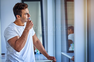 Buy stock photo Shot of a handsome young man looking thoughtful while brushing his teeth at home