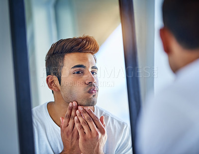 Buy stock photo Shot of a handsome young man admiring looking at his face in the bathroom mirror