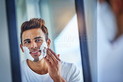 Buy stock photo Shot of a handsome young man shaving his facial hair in the bathroom