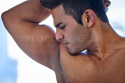 Buy stock photo Shot of a handsome young man smelling his armpits during his morning grooming routine