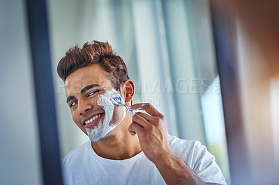 Buy stock photo Shot of a handsome young man shaving his facial hair in the bathroom