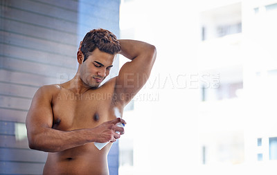 Buy stock photo Shot of a handsome young man spraying himself with deodorant