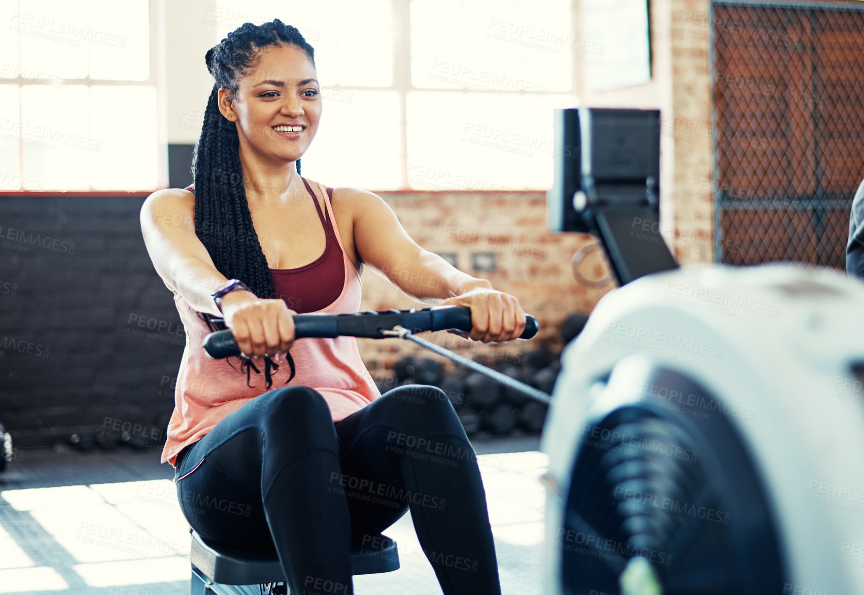 Buy stock photo Shot of a happy young woman working out on a rowing machine