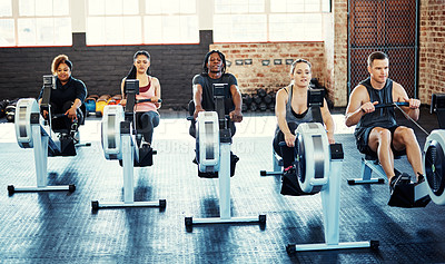 Buy stock photo Shot of a fitness group working out on rowing machines in their session at the gym