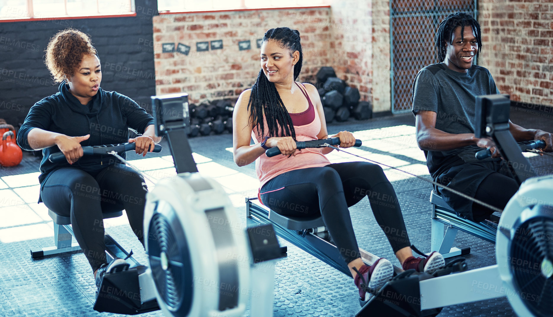 Buy stock photo Shot of a fitness group working out on rowing machines in their session at the gym