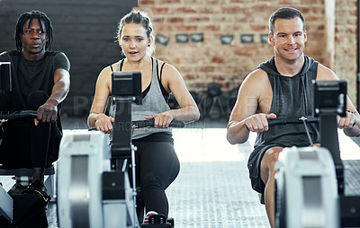 Buy stock photo Shot of a fitness group working out on rowing machines in their session at the gym