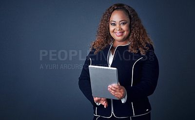 Buy stock photo Portrait of a confident young businesswoman working on her digital tablet while standing against a blue background