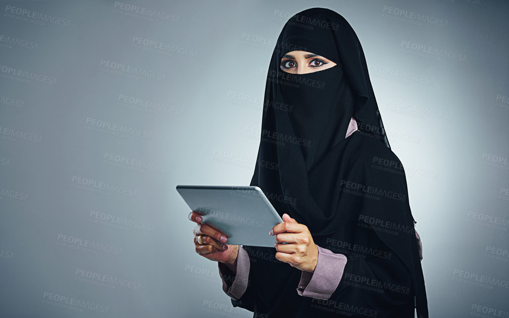 Buy stock photo Studio portrait of a young woman wearing a burqa and using a digital tablet against a gray background