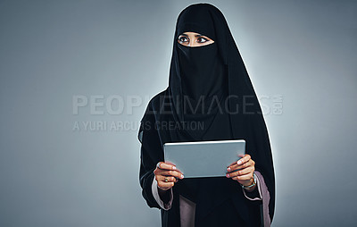 Buy stock photo Studio shot of a young woman wearing a burqa and using a digital tablet against a gray background