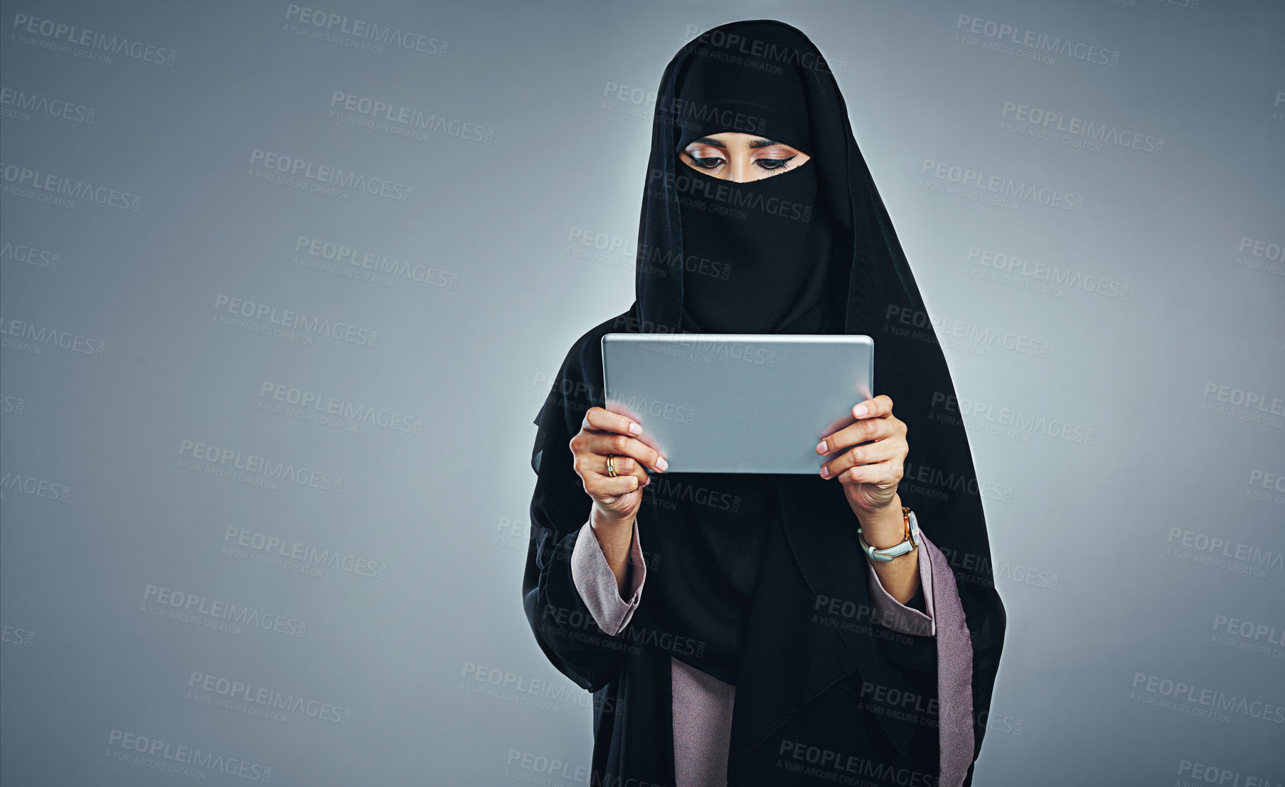 Buy stock photo Studio shot of a young woman wearing a burqa and using a digital tablet against a gray background