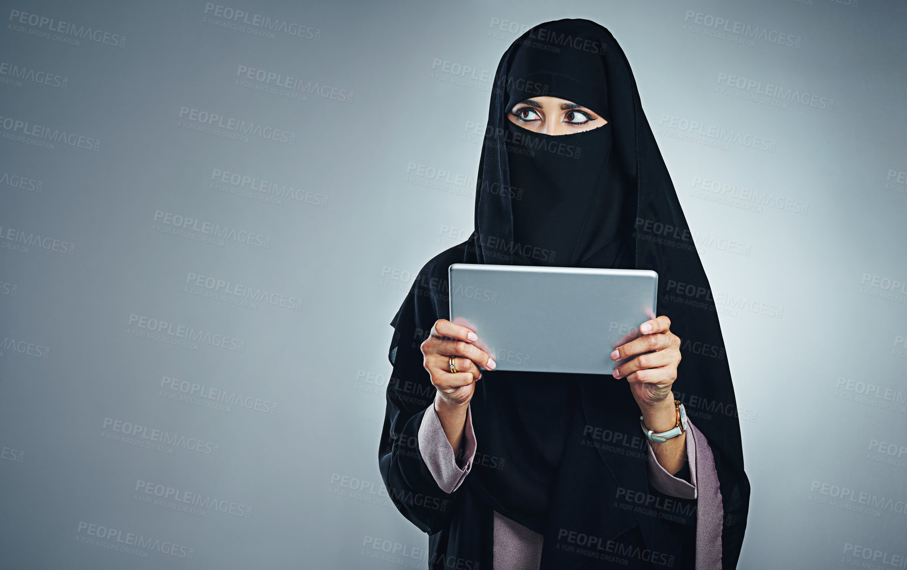 Buy stock photo Studio shot of a young woman wearing a burqa and using a digital tablet against a gray background