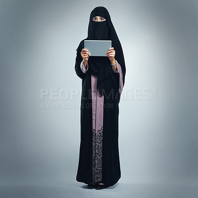 Buy stock photo Studio portrait of a young woman wearing a burqa and using a digital tablet against a gray background