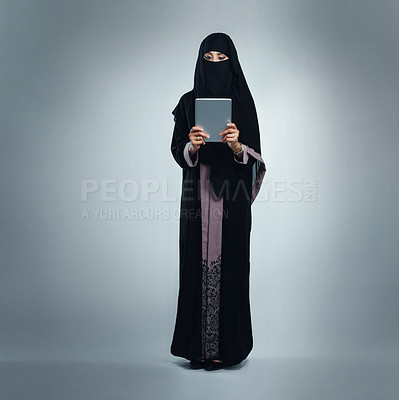 Buy stock photo Studio shot of a young woman wearing a burqa and using a digital tablet against a gray background