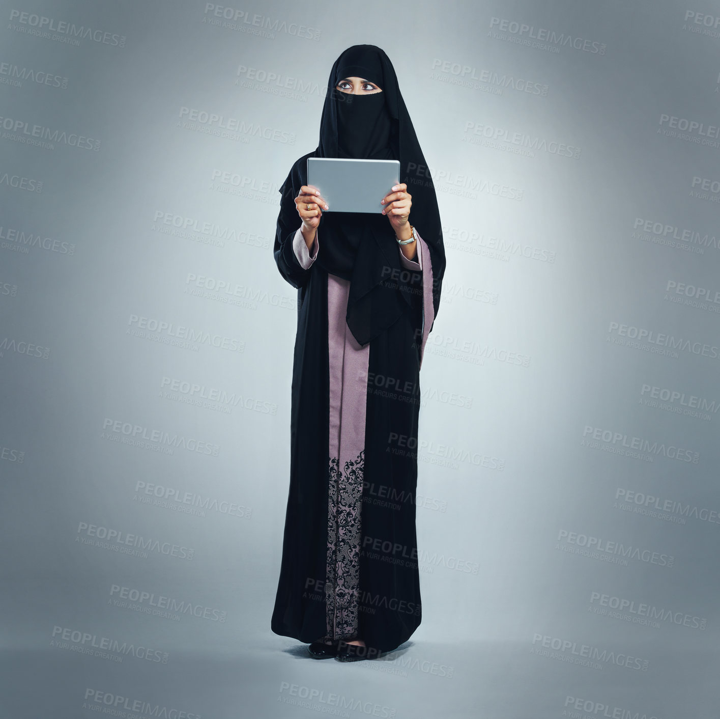 Buy stock photo Studio shot of a young woman wearing a burqa and using a digital tablet against a gray background