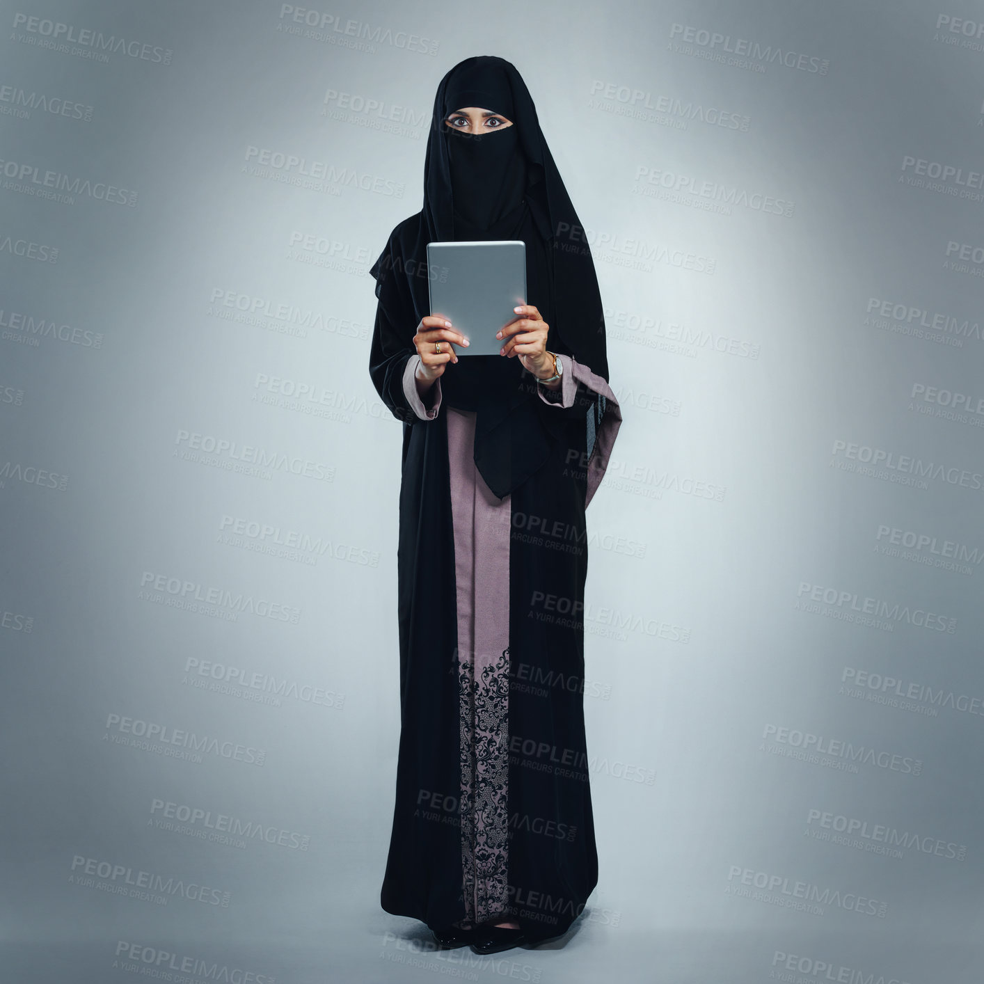 Buy stock photo Studio portrait of a young woman wearing a burqa and using a digital tablet against a gray background