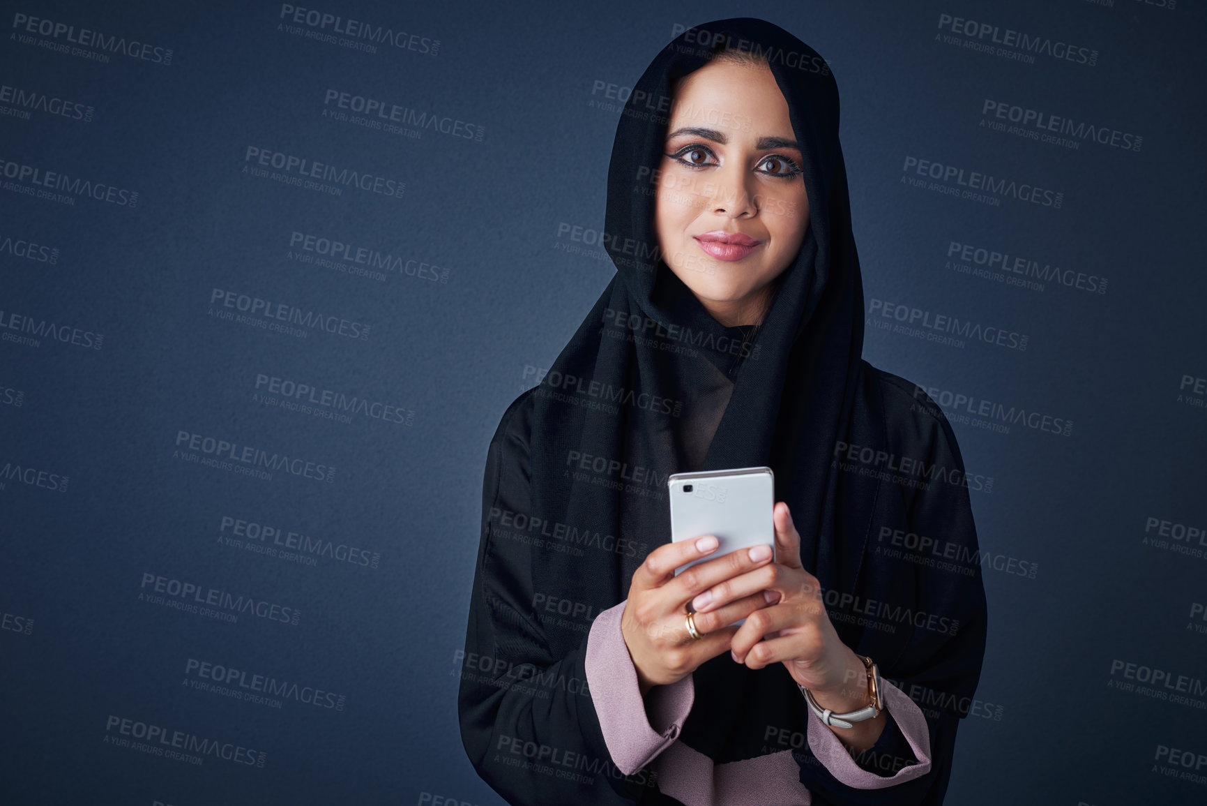 Buy stock photo Studio portrait of a young woman wearing a burqa and using a mobile phone against a gray background