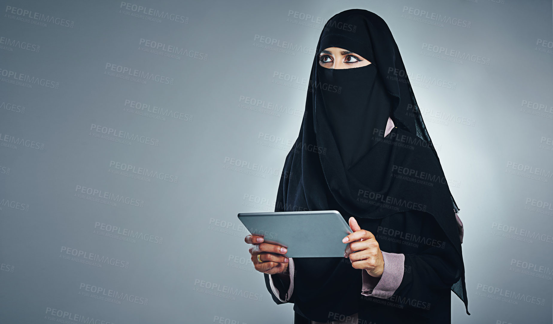 Buy stock photo Studio shot of a young woman wearing a burqa and using a digital tablet against a gray background