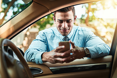 Buy stock photo Shot of a young businessman using a cellphone while leaning against his car