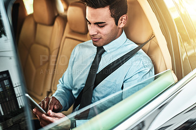 Buy stock photo Shot of a young businessman using a digital tablet while sitting in the back seat of a car
